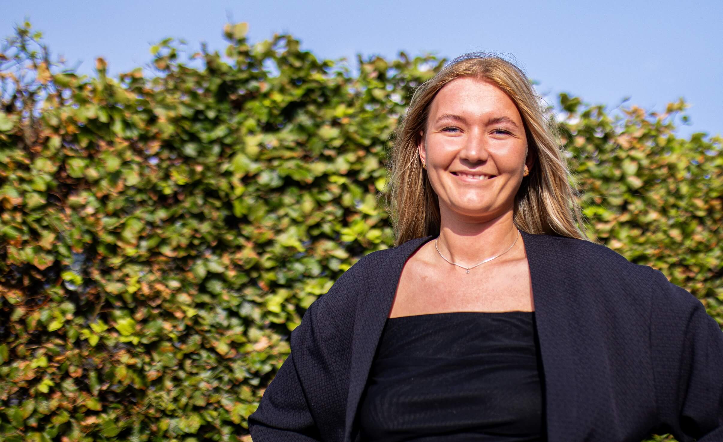 Celina smiler til kameraet ude foran busk